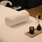 A serene spa massage table setup with a rolled towel, candle, and decorative vases in a relaxing environment.