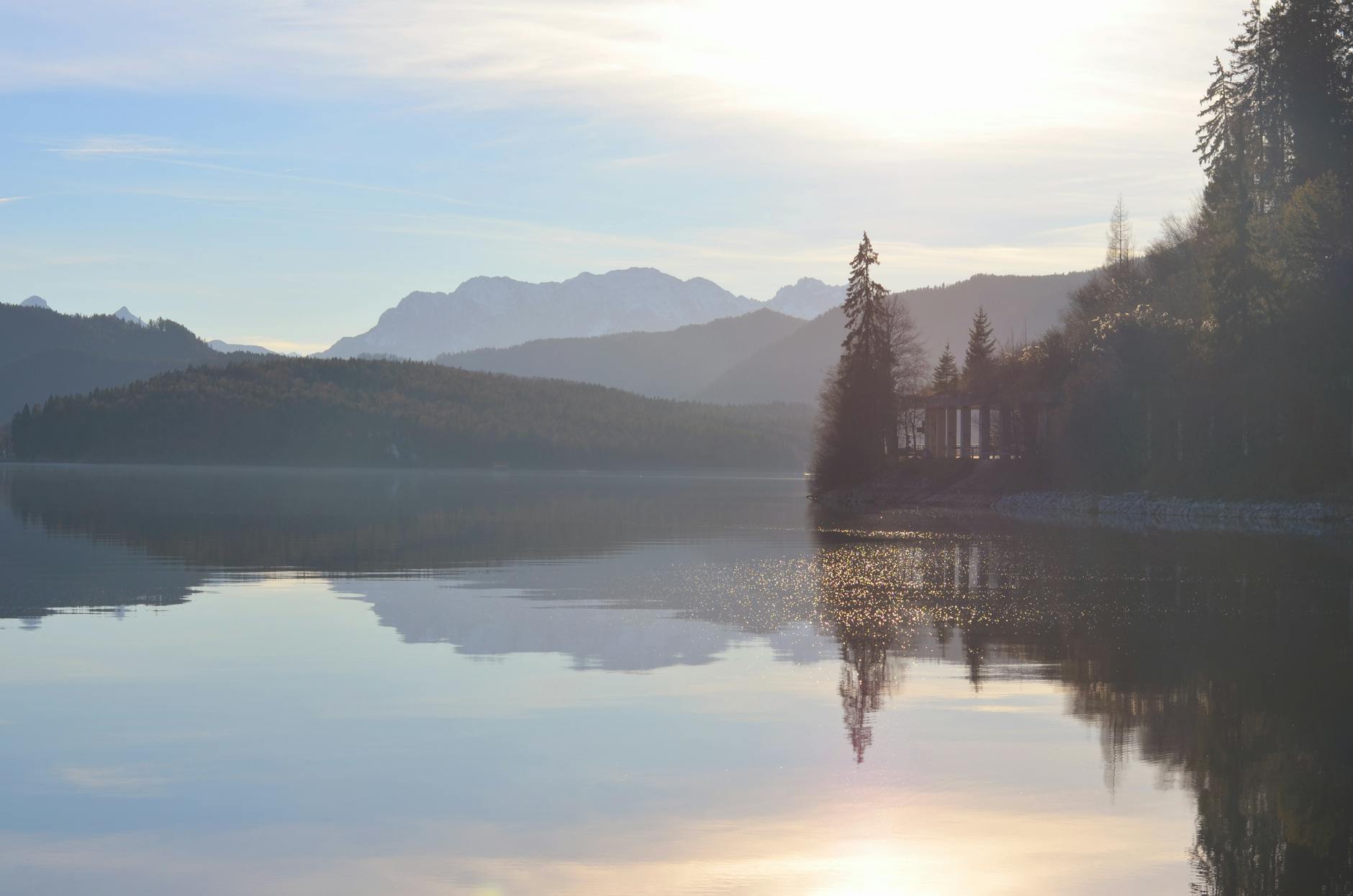 A tranquil mountain lake reflecting trees and mountains at sunset, creating a calm and peaceful scene.