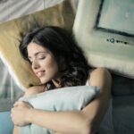 Woman peacefully sleeping in bed, hugging a pillow with a contented smile.