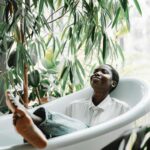 A black woman enjoys relaxation in a bathtub surrounded by lush green plants, embracing self-care.