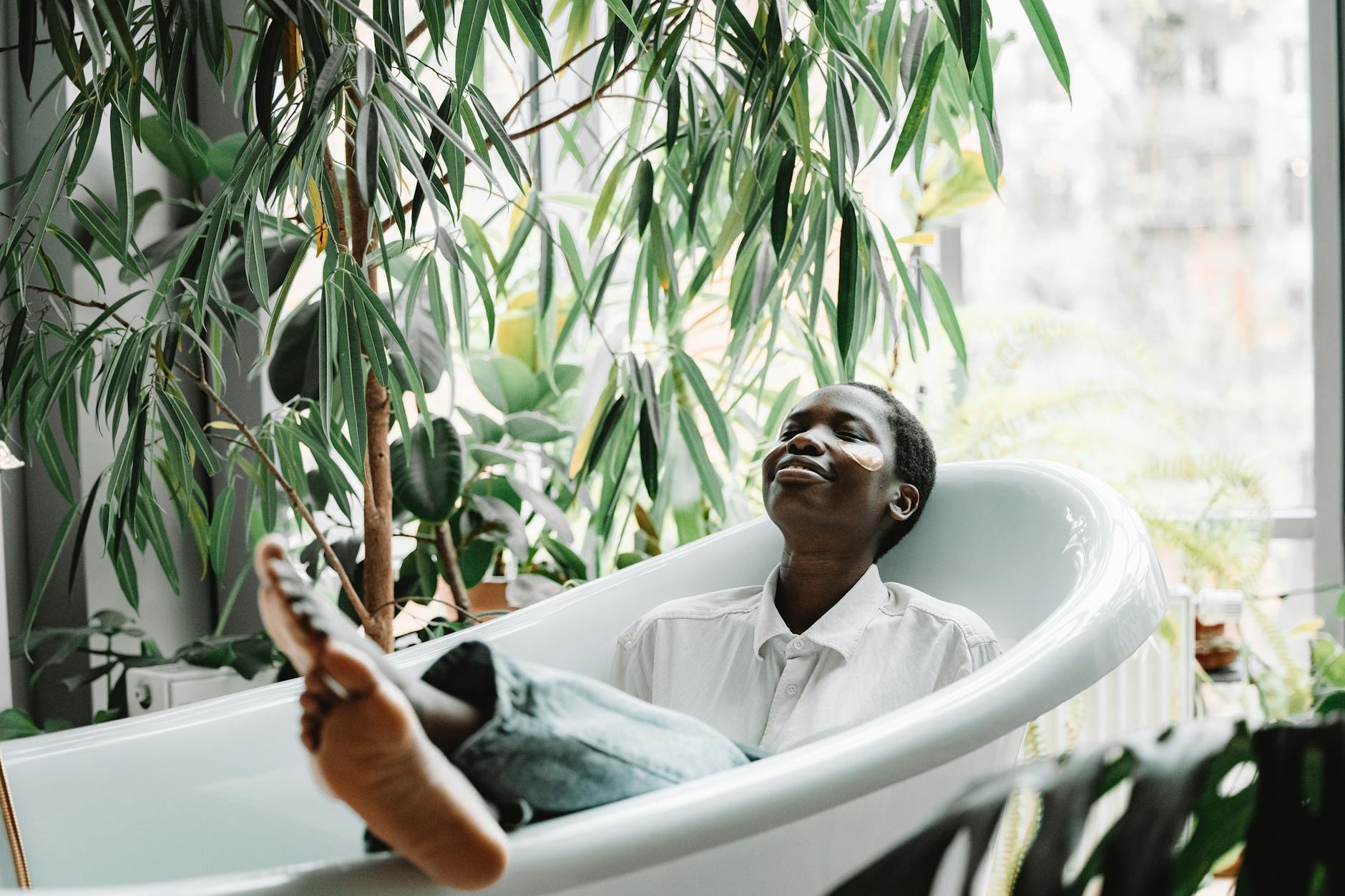 A black woman enjoys relaxation in a bathtub surrounded by lush green plants, embracing self-care.