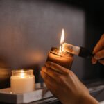 Close-up of hands lighting candles indoors, creating a warm cozy ambiance.