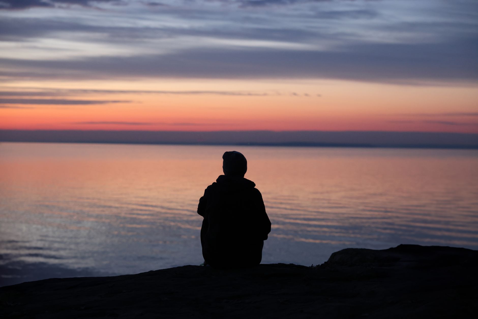 A contemplative silhouette of a person sitting by the calm sea during a beautiful sunset.