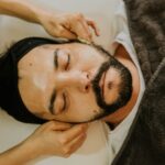 Close-up of a man receiving a facial massage with eyes closed, promoting relaxation and skincare.