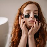Woman with red hair enjoying a skincare routine with under-eye masks indoors.